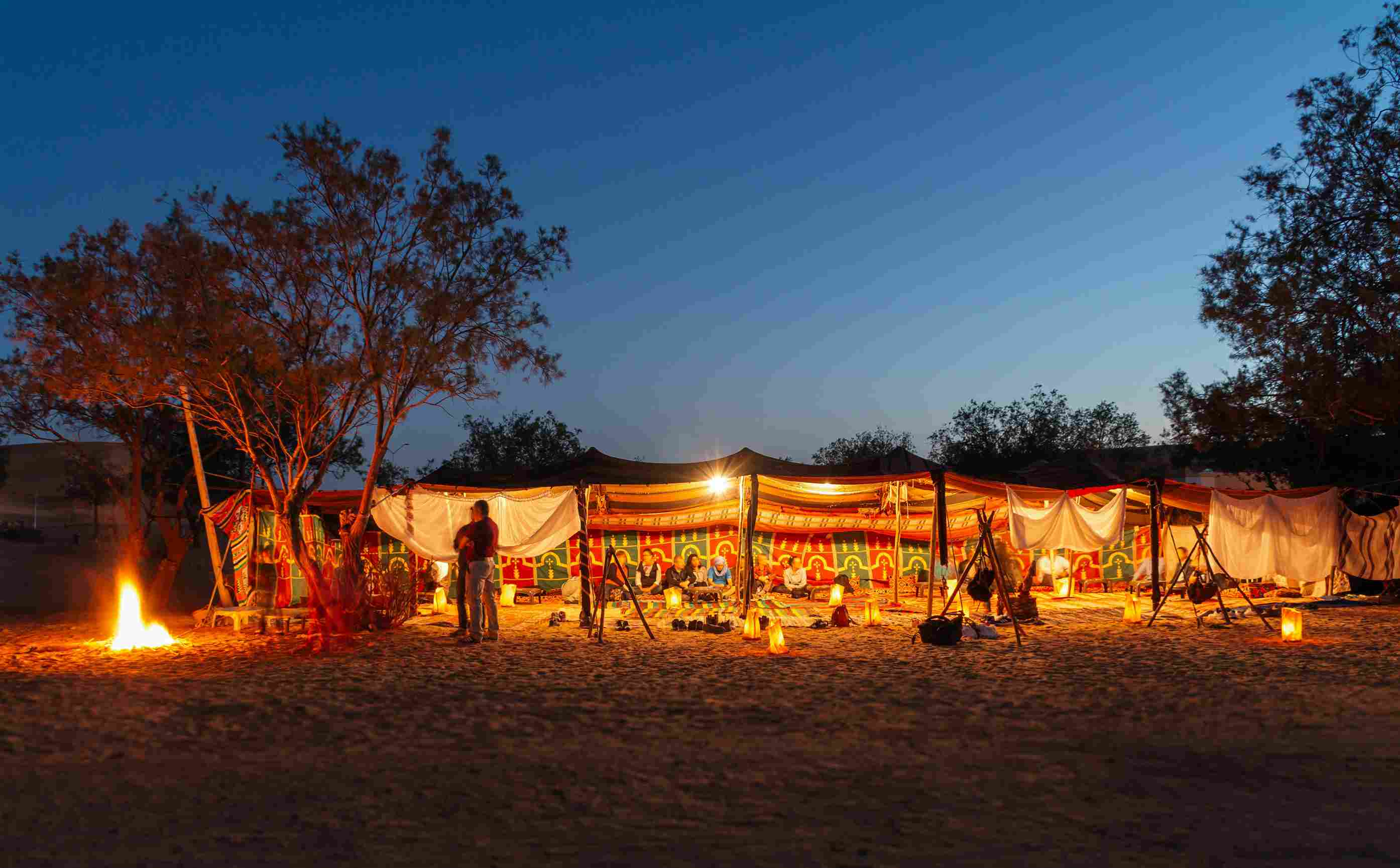 A well-lit campsite at night with bonfire and two people.